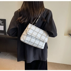 Détail d'un sac à bandoulière en tweed blanc avec chaîne dorée porté par un mannequin