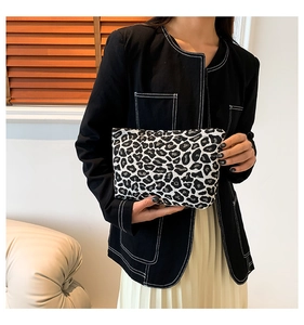 Fashionable leopard print clutch bag held by model in a cozy interior setting