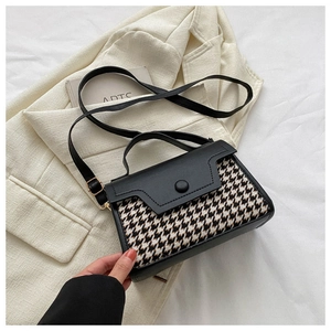 Detail der Vintage-Hahnentritt-Handtasche mit schwarzer Lederklappe auf beigem Blazer