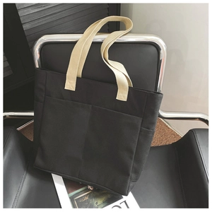 Détail du grand sac cabas en toile noire avec anses beiges sur une chaise en cuir