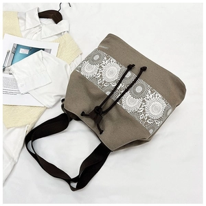 Detail of khaki canvas bucket bag featuring floral lace patterns and drawstring closure