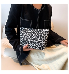 Detail of a chic leopard print canvas clutch held against a minimal black and white outfit
