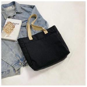 Détail du sac cabas en toile noire avec anses marron clair et poches latérales