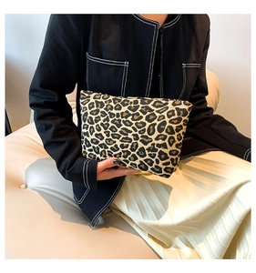 Fashionable leopard print fabric clutch bag held by model against a cream leather sofa