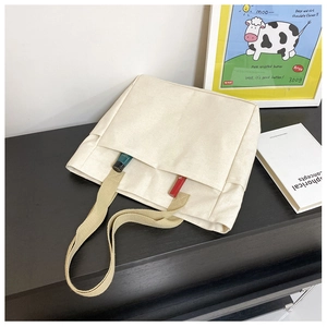 Détail du sac cabas en toile blanc cassé montrant la poche avant et les poignées