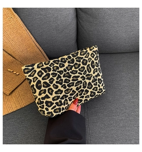 Detail of leopard print clutch bag made of jacquard fabric held against a grey sofa