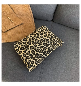 Detail view of leopard print clutch bag with golden metal zipper on a dark sofa