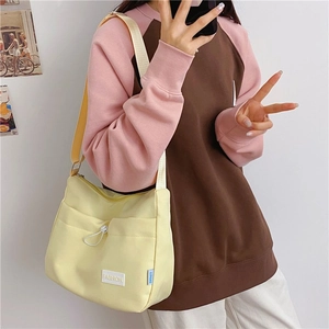 Detail of light yellow canvas shoulder bag with front drawstring pocket and fashion label