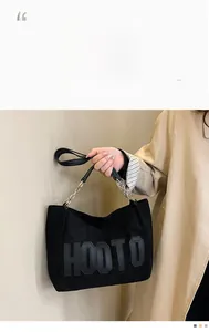 Detail of black plush tote bag featuring HOOTO lettering and metal chain handle