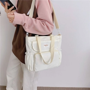 Close-up of white canvas tote bag with multiple functional pockets and adjustable strap