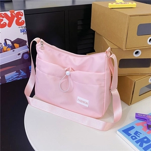 Pink nylon crossbody bag with drawstring pocket and adjustable strap on white table