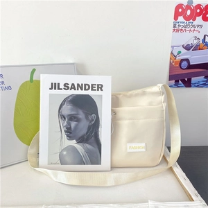 Detail of beige nylon dumpling bag with fashion label and front pocket in lifestyle setting