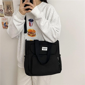 Detail view of black canvas tote bag showing multiple pockets and adjustable strap
