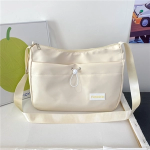 Close-up detail of cream nylon shoulder bag featuring a front pocket and fashion label