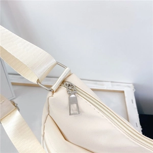 Detailed view of the smooth zipper closure and silver metal rings on a cream nylon bag