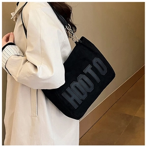 Detail of a black plush tote bag featuring embossed letters and a metal chain strap