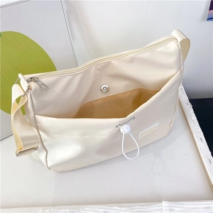 Detail view of cream nylon crossbody dumpling bag with adjustable strap and front pocket