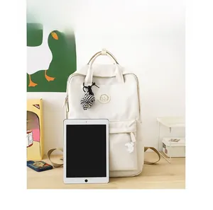Detailed view of cream nylon backpack with tablet for size reference and cute plush charms