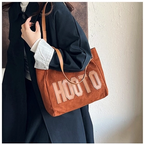 Brown plush tote bag with embroidered HOOTO letters shown worn with a dark trench coat