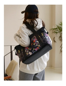 Detail view of large capacity floral travel bag with shoulder strap worn by a model