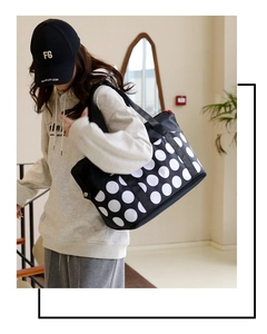 Detail shot of black tote bag with white polka dots, red zipper and metal side buckle