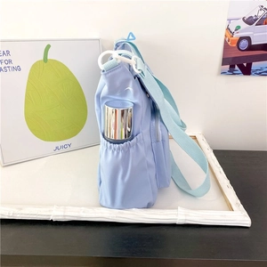 Detail of light blue crossbody bag featuring a side drawstring pocket with water bottle