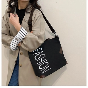Detail of black canvas tote bag with FASHION lettering and brown leather corners