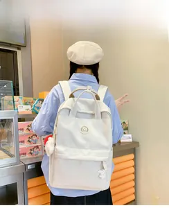 White minimalist backpack with plush pendant and mountain logo shown on a model