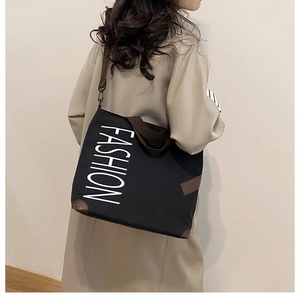 Detail view of black canvas fashion tote bag showing leather corner patches and brown strap