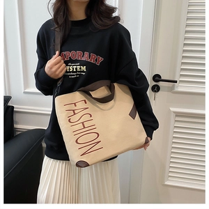 Detail of a large beige canvas tote bag with brown straps and bold fashion print text