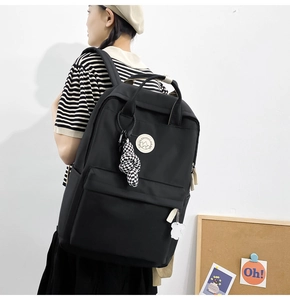 Detail of black nylon backpack featuring front zipper pocket and checkered knot charm