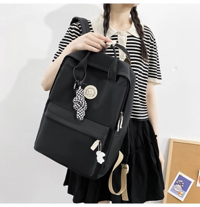 Detail of black nylon backpack featuring checkered knot charm and cute white bear pendant