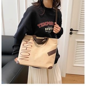 Detail of canvas tote bag with brown handles and fashion print worn by a model