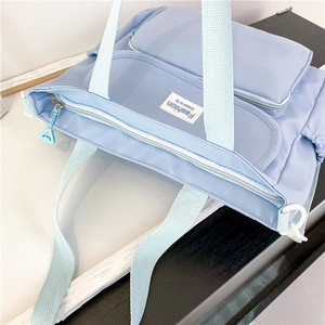 Detail view of light blue nylon tote bag showing zipper closure and fabric handles