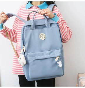 Close-up of light blue casual backpack with plush ball and cartoon dog charms attached
