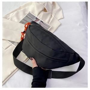 Detail of black nylon crescent bag featuring a vibrant orange chain charm and wide strap