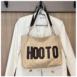 Close-up of beige plush tote bag with brown HOOTO letters and chain leather strap