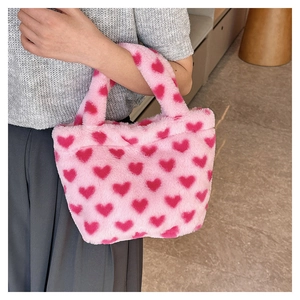 Close-up of soft pink plush handbag featuring cute red heart patterns for autumn and winter