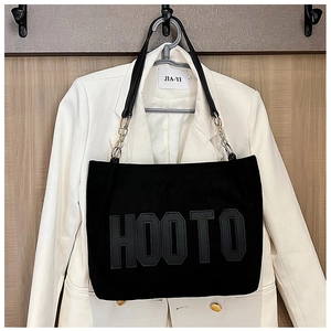 Close-up of large black plush tote with HOOTO letters and metal chain strap details