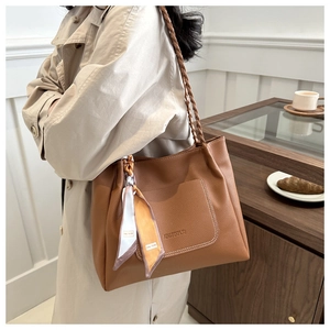 Dettaglio di una borsa a secchiello in pelle marrone con spalline intrecciate e foulard