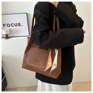 Dettaglio borsa tote marrone in pelle con manico intrecciato e accessorio foulard in seta