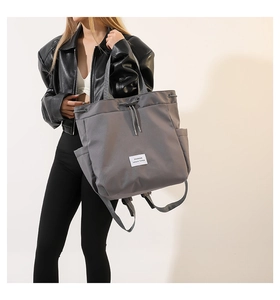 Detail of grey nylon tote bag with drawstring closure and fashion woven label on front
