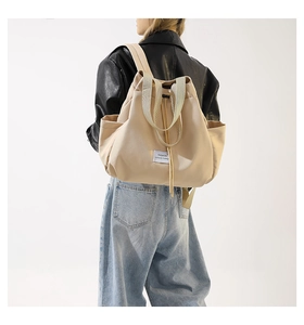 Detailed back view of a beige nylon drawstring backpack worn by a model in casual outfit