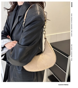 Detail of beige felt half-moon shoulder bag with gold metal chain strap on black leather jacket
