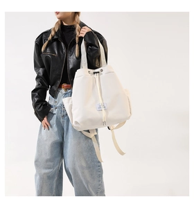 Detail of white nylon drawstring tote bag with adjustable straps and blue brand label