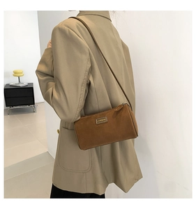 Détail d'un sac cylindrique en daim marron avec logo en métal et fine bandoulière