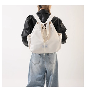 Detailed side view of white nylon drawstring backpack with side pocket and blue fabric label