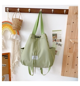 Detail view of light green nylon drawstring backpack with brand label on wooden hook