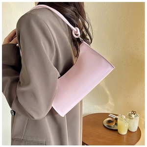 Détail du sac baguette en cuir verni rose clair avec nœud stylé sur la bandoulière