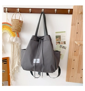 Detail of grey nylon drawstring bag with white woven label on a wooden hook